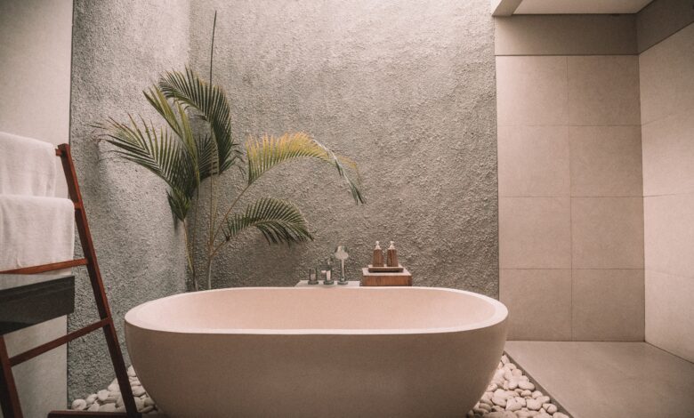 Salle de bain de couleur, doté d'un mur qui fait penser aux grains de sable de la plage, une baignoire posé sur des cailloux de mer, un pot de fleur avec un petit palmier rappelant la plage