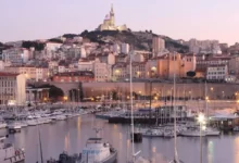 Vue panoramique d'un port rempli de nombreux bateaux à côté d’une ville de Marseille avec des immeubles résidentiels et commerciaux en arrière-plan, reflétant le dynamisme du marché immobilier local.
