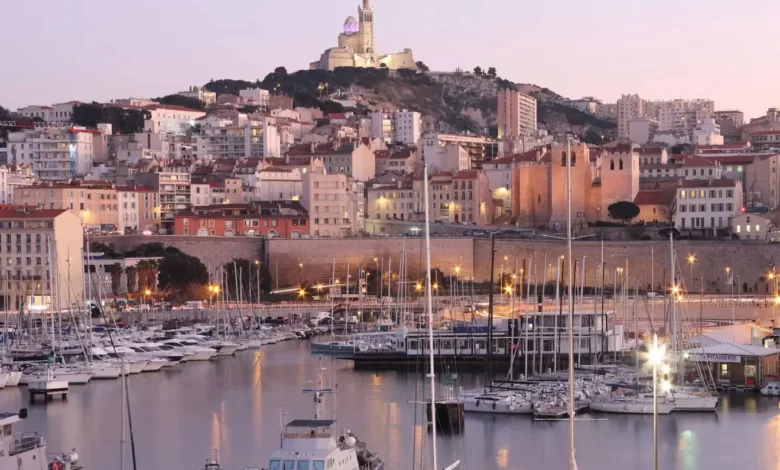 Vue panoramique d'un port rempli de nombreux bateaux à côté d’une ville de Marseille avec des immeubles résidentiels et commerciaux en arrière-plan, reflétant le dynamisme du marché immobilier local.